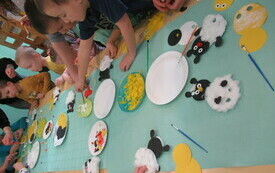 Przy stole grupa dzieci wykonuje baranki oraz kurczaczki z artykuł&oacute;w papierniczych oraz dekoracyjnych. 