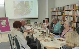 Członkowie klubu miłośnik&oacute;w książek podczas spotkania zdjęcie begonii kr&oacute;lewskiej wyświetlane na ekranie projekcyjnym.