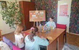 Dziewczynki siedzą przy stoliku i wykonują pracę plastyczną.