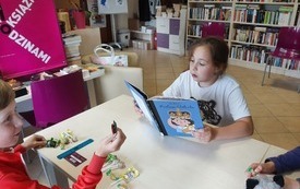 Dziewczynka trzyma w ręku książkę i czyta.