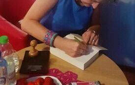Kobieta w niebieskiej sukience składa autograf w książce.