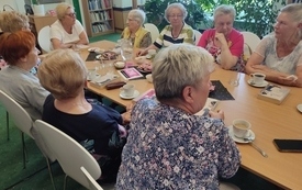 Grupa kobiet w średnik wieku siedzi wokół stoły i rozmawiają.