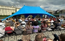 Uczestnicy spotkania autorskiego siedzą na krzesełkach pod niebieskim namiotem.