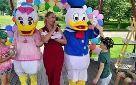 Maskotki Kaczora Donalda i Kaczki Daisy, a pośrodku bibliotekarka prowadząca wydarzenie. W tle kolorowe balony. 