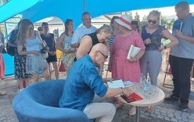 Pisarz podpisujący książki oraz czytelnicy stojący w kolejce po autograf. 
