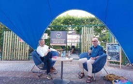 Dw&oacute;ch mężczyzn siedzących na niebieskich fotelach, prowadzących rozmowę. 