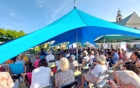 Pod niebieskim namiotem publiczność zgromadzona na spotkaniu autorskim. 
