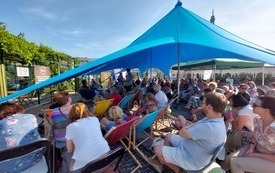 Publiczność zgromadzona na spotkaniu siedząca pod niebieskim namiotem. 