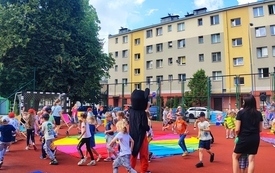 Grupa dzieci bawi się na boisku z kolorową chusta i postacią Myszki Miki