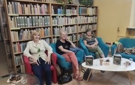 Trzy kobiety siedzą na fotelach. Za nimi ściana z książkami.