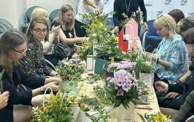 Wok&oacute;ł stołu z ziołami i kwiatami kobiety uczestniczące w warsztatach florystycznych.
