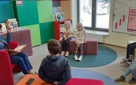 Kilka dzieci siedzi na dywanie i patrzą na prowadzącą spotkanie.