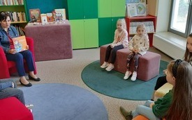 Kobieta czyta książkę, dzieci słuchają.