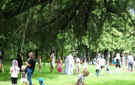 Dzieci i dorośli bawią się wsp&oacute;lnie na trawniku w parku