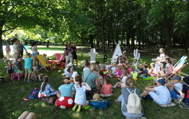 Grupa dzieci i dorosłych bawi się wsp&oacute;lnie na trawniku w parku