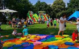 Dzieci bawią się na dmuchanych zabawkach i kolorowych poduszkach rozłozonych na trawie w parku