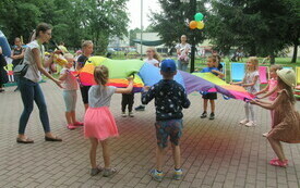 Grupa dzieci stoi trzymając wsp&oacute;lnie wielką kolorową chustę