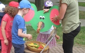 Dzieci stoją przy koszyku wypełnionym owocami i warzywami