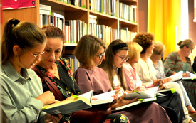 Grupa kobiet siedzi i trzyma w rękach książki. W tle regały z książkami.