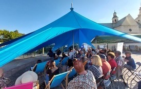 Publiczność zgromadzona na spotkaniu w Ogrodach Bernardyńskich siedząca pod niebieskim namiotem.