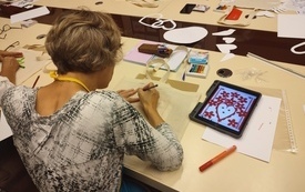 Uczestniczka warsztatów podczas projektowania wzoru lasowiackiego. Na stole tablet, kartki papieru, ołówki i szablony.
