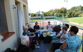 Grupa kobiet na tarasie siedzi na fotelach i rozmawia.