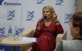Pisarka w blond włosach i czerwonej sukience przemawia do mikrofonu.