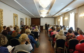 Po dwóch stronach sali konferencyjnej rzędy krzeseł, na których siedzą kobiety.