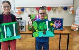 Dziewczynka i chłopiec w okularach prezentują prace o tematyce leśnej.