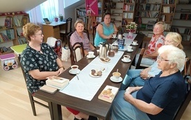 Sześć kobiet siedzi wok&oacute;ł stołu, w tle regały z książkami.