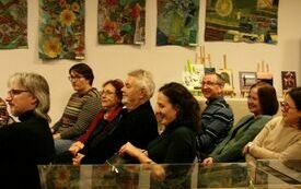 Grupa os&oacute;b dorosłych siedzi w pomieszczeniu z obrazami na ścianie