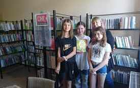 Trzy dziewczynki  i bibliotekarka stoją obok siebie, Wokół regały z ksiązkami.