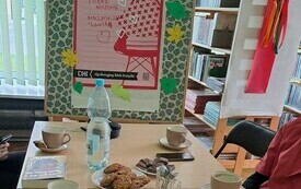 Na stoliku książki, filiżanki i tablica obok z logo DKK.
