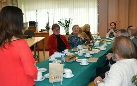 Grupa ludzi siedzi przy stole, na pierwszym planie stoi bokiem dyrektor biblioteki w Ropczycach.