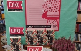 Na stole kilka książek, wrzosy, w tle plakat Dyskusyjnych Klubów Książki.