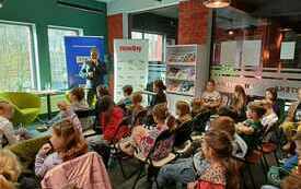 Dzieci uczestniczą w spotkaniu autorskim. Pisarz przemawia do mikrofonu.