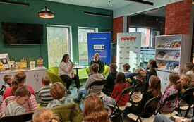 Wnętrze biblioteki wypełnione dziećmi siedzącymi na krzesłach.