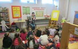 Bibliotekarka czyta książkę dzieciom siedzącym na dywanie.