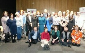 Uczestnicy konferencji, kobiety i mężczyźni w różnym wieku pozują do wspólnej fotografii.