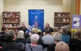 W tle regały z książkami, na tle bibliotecznego logo siedzą dwie kobiety i prowadzą rozmowę.
