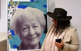 Plakat z Wisławą Szymborską, obok niego stoi kobieta w kapeluszu. 