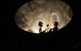 Przedstawienie w formie teatru cieni: posiać mężczyzny i kobiety, pośrodku nich kwiat r&oacute;ży