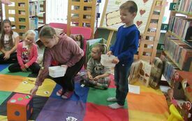 Dzieci grają w gre na kolorowej macie w bibliotece.