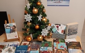 Na stoliku książki o tematyce świątecznej i choinka udekorowana złotymi bombkami i białymi gwiazdkami.