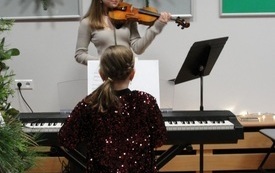 Młoda dziewczyna gra na klawiszach. Obok dziewczyna gra na skrzypcach.