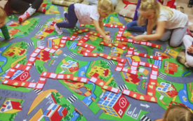 Na dywanie siedzą dzieci i grają w grę papierowe domino. 