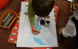Chłopiec w zielonej bluzie rysuje kredkami oł&oacute;wkowymi. 