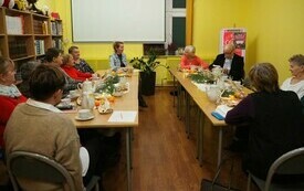 Kilkanaście osób siedzi na krzesłach i słucha osoby do nich mówiącej.
