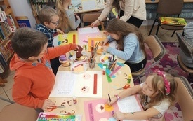 Dzieci siedzące przy stole wykonują prace plastyczne