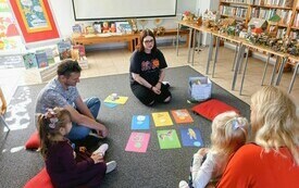 Bibliotekarka prowadzi zajęcia z dziećmi. Siedzą na dywanie. 
